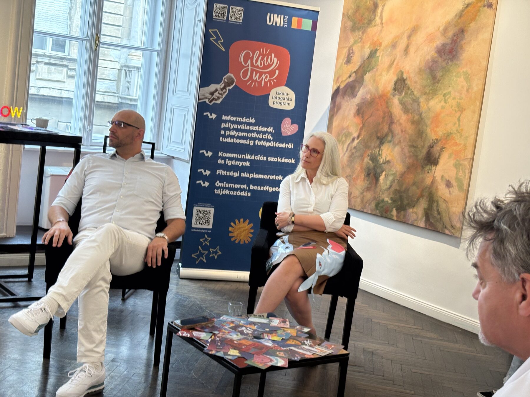 Két beszélgetőpartner a karosszékekben a rendezvénybanner mellett